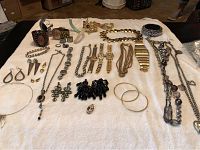 Full view of the assortment of costume jewelry laid out on white surface showing watches, necklaces, bracelets, earrings, and brooches.