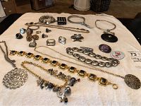 Overview of all costume jewellery laid out on white cloth, showing necklaces, rings, brooches and bracelets in silver and gold tones, some with colored stones.