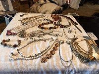 Wide view of assortment of vintage costume jewelry laid on cloth, mainly necklaces with varied beads and chains.
