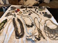 Wide view showing nearly 30 pieces of vintage costume jewelry arranged on white cloth including necklaces, rings, brooches, and a watch