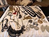 Overall view of approximately 30 costume jewelry pieces spread on surface, showing variety of necklaces, bracelets, pendants, and rings.