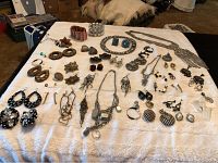 Wide overview of approximately 30 pieces of costume jewelry laid out on a white surface, showing earrings, rings, bracelets, and necklaces from the 70s-80s era.