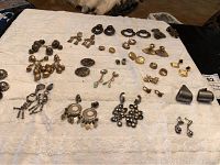 Wide view of over 20 pairs of costume jewelry earrings laid out on white cloth. Includes various styles in gold and silver tones, clip-ons and pierced, with detailed metal work and some bead embellishments.