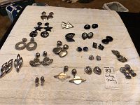 Photo of laid out 20 pairs of various costume costume earrings in silver-tone and black finishes, showing different shapes and styles including studs and dangles.