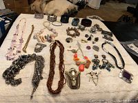 Full overview of assorted costume jewelry spread on a white cloth, showing necklaces, bracelets, brooches and earrings.
