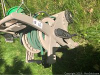 Photo showing beige garden hose reel with green hose coiled around it, on grass