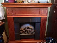 Front view of wood electric fireplace with decorative paneling and faux log insert.
