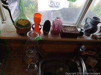 Window sill with oil lamp, carved wooden box, glass vases, and other decorative items