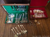 Two wooden boxes containing various pieces of flatware, serving utensils, and napkin rings spread out on wood floor.