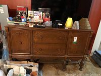 Front view of vintage oak highboard cabinet with items on top, showing carved doors, drawers, and wooden knobs.