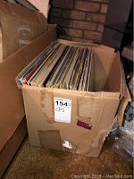Closed box packed with about thirty assorted LP records with visible wear on cardboard box
