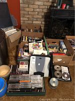 Box and binder filled with jewel cases and binders containing CDs and DVDs without discs, along with loose discs and burned discs in sleeves.