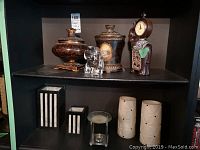 Shelf with decorative clock, two lidded jars, and clear glass elephant figurine.