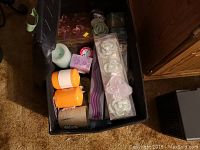 Black storage box with assortment of candles including pillar, decorative shaped, and tray candles.