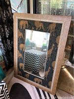 Frontal photo showing the full mirror with animal print frame, featuring elephants, lions, and giraffes on dark background, and a beige crackled outer border.