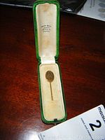 Vintage 10K gold stick pin displayed inside an open green velvet-lined case on a wooden surface with jeweler's name inside the lid.