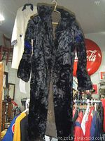 Front view of long black fur coat hanging on a hanger, showing full coat length.