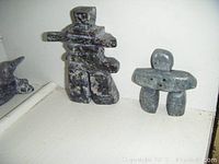 Photo showing the two soapstone Inuksuk figures side by side on a white surface showing their relative size and detail.