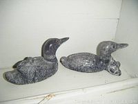 Two carved loons with babies in soapstone, dark stone with detailed etched feathers and red eyes, photographed side by side on a white surface.