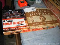 Photo of G.I. Joe Combat Infantry game box alongside vintage picture puzzle box on a table surface.