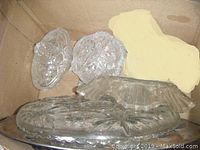 Box with multiple clear glass items including covered dishes, serving platters, and decorative pieces showing pressed pinwheel patterns