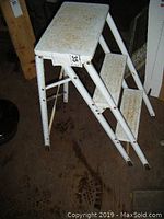 Side view of the vintage white metal 2-step stool with seat, showing tubular legs and two steps with minor surface rust.