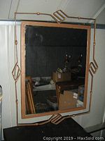 Full view of rectangular mirror hanging on wall, showing metal frame with geometric design and reflective surface.