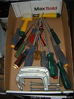Photo showing various screwdrivers and two C-clamps in a box.