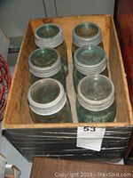 Box containing six aqua-colored vintage glass sealer jars with metal lids, showing top view with lids on, arranged in two rows inside a wooden box.