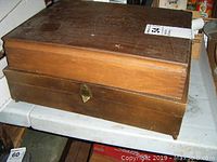 Top and front view of a vintage wooden cutlery chest with a brass latch, showing signs of surface wear.