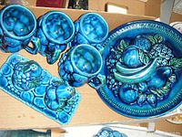 Overhead photo showing 4 blue mugs, condiment dish, salt and pepper shakers, and a large decorative fruit motif plate.