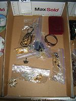 Overview of tray containing various pieces of costume jewelry, some loose and some in plastic bags, including brooches, bracelets, necklaces, pins, earrings, and a ring.