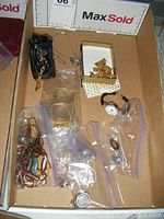 Tray of assorted costume jewelry showing multiple items including watches, bracelets, necklaces, brooches, and pins within a cardboard box.