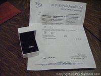 Ring and accompanying appraisal certificate displayed in black jewelry box on wooden surface