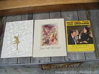 Three items laid out on wood surface: white skating programme with gold embossed skater, Gone With The Wind vintage programme with illustrated characters and Confederate flag, and a yellow-covered 1940 edition book of Gone With The Wind.