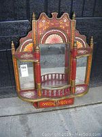 Front view of vintage hand painted wooden wall cabinet showing three mirrors, floral decorations, and small drawer at bottom.