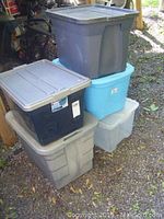Stack of five medium-sized storage totes, showing variety of colors and lids, some with wear and dust.