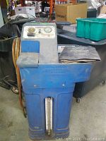 Blue vintage Wynn's Powerflush machine with control panel, pressure gauge, and hoses attached. Unit is standing on a concrete floor in a workshop environment.