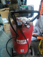 Photo of a red vertical Porter Cable air compressor with black handle, pressure gauges, and wheels. Shows brand label and components.