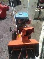 Front view of Sears 8/24 snowblower showing the orange auger housing, blue fuel tank, red pull start mechanism, tires, and white handle bars.