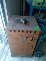 Front top view of rusted vintage welding machine showing vent holes and black knob on lid.