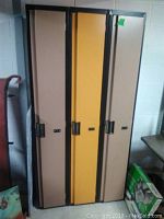 Section of three metal lockers, two brown and one yellow, showing front closed doors with handles and locks.
