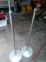 Full view of the two vintage microphone stands showing their height and round metal bases on concrete floor.