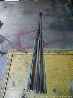 Full view of two collapsed vintage metal Atlas Sound speaker stands lying on ground showing extended legs and central pole with clamps.