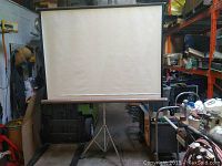 Vintage Dalite projection screen extended and supported on tripod stand, showing full screen and roller mechanism.