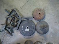 Lot showing three round weighted metal stand bases and a set of metal mounting brackets and hardware on a concrete floor.