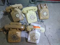 Five rotary dial telephones in different beige and off-white shades, arranged on floor showing dials and handset cords.