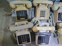 Top view of four vintage DTMF telephones arranged in two rows on a flat surface, showing beige/cream plastic housings, push-button keypads, coiled cords, and corded handsets.
