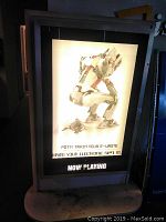 Front view of the illuminated movie poster display panel showing a movie poster and 'NOW PLAYING' signage at bottom.
