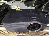 Front view showing black Optoma projector with lens on right side, top controls and ribbed side panels